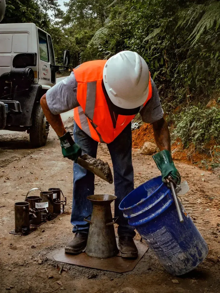 Técnico do Laboratório HCT coletando amostra de concreto em obra, ao lado do caminhão betoneira, com o cone de abatimento e os moldes de corpo de prova sobre a placa